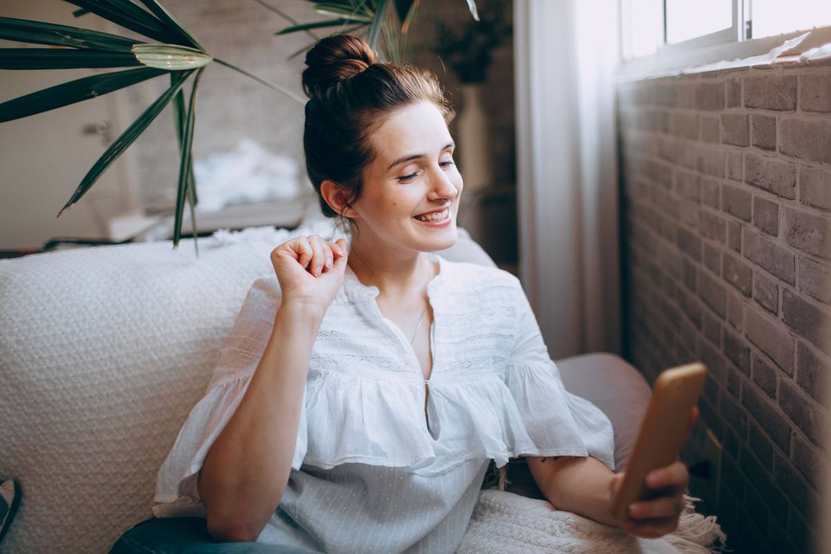 A woman smiling at her phone on a sofa